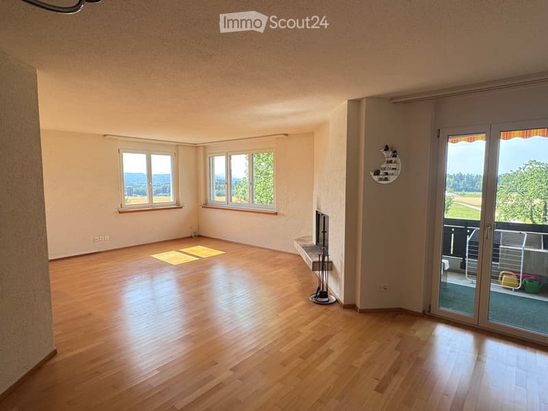 Empty room with wooden flooring, large windows offering a scenic view, and a sliding glass door leading to a balcony.