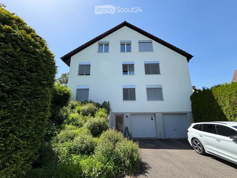 Two-story house with white exterior, multiple windows, garage, and a parked car in front.