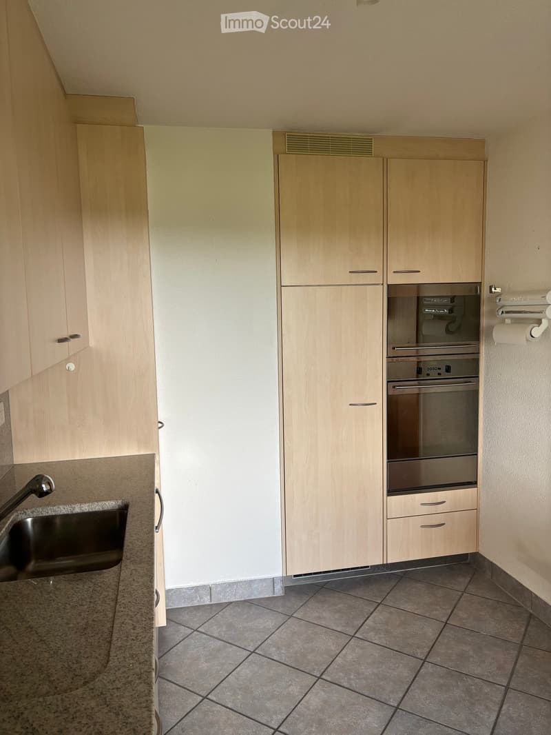 Modern kitchen with light wood cabinets, stainless steel oven, granite countertop, and tiled floor.