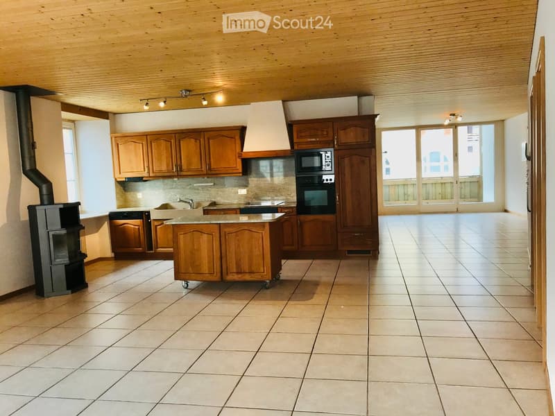 Bright kitchen with wooden cabinets, a central island, and modern appliances including an oven and microwave. Features a tiled floor, large windows, and a wood-burning stove.