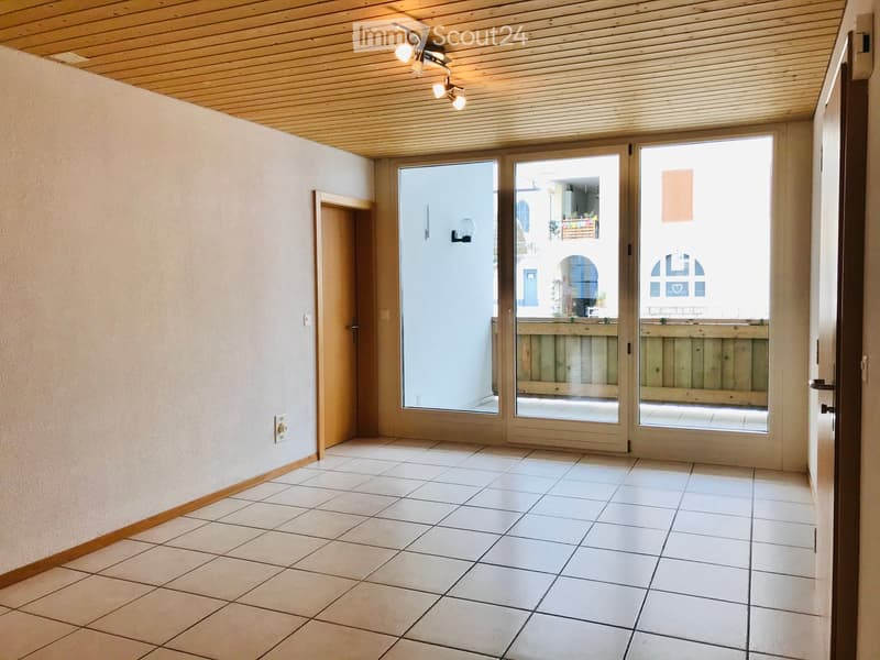 Empty hallway with tiled floor, white walls, wooden ceiling, and large glass doors leading to an outdoor area.