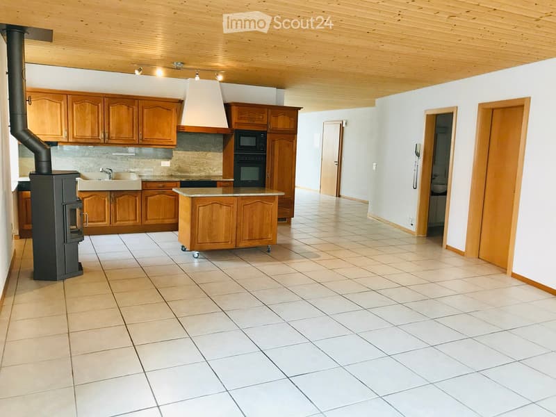 Bright, modern kitchen with wooden cabinets, a central island, a stove, sink, microwave, and oven. The space features tiled flooring and a wooden ceiling.