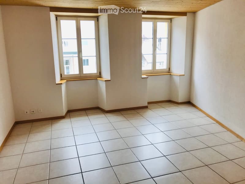 Empty room with tiled floor, white walls, and large windows with wooden sills.
