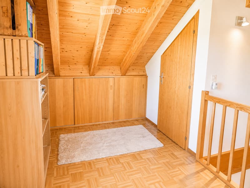 Bright hallway with wooden flooring, white walls, and a wooden door leading to another room. Features built-in wooden cabinets and a small white rug on the floor.