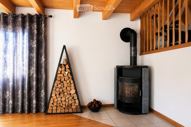 A cozy room with a modern black fireplace, a wooden woodpile, and a decorative curtain on the left side.