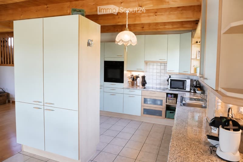 Modern kitchen with light-colored cabinets, stainless steel appliances, granite countertops, and a hanging light fixture.