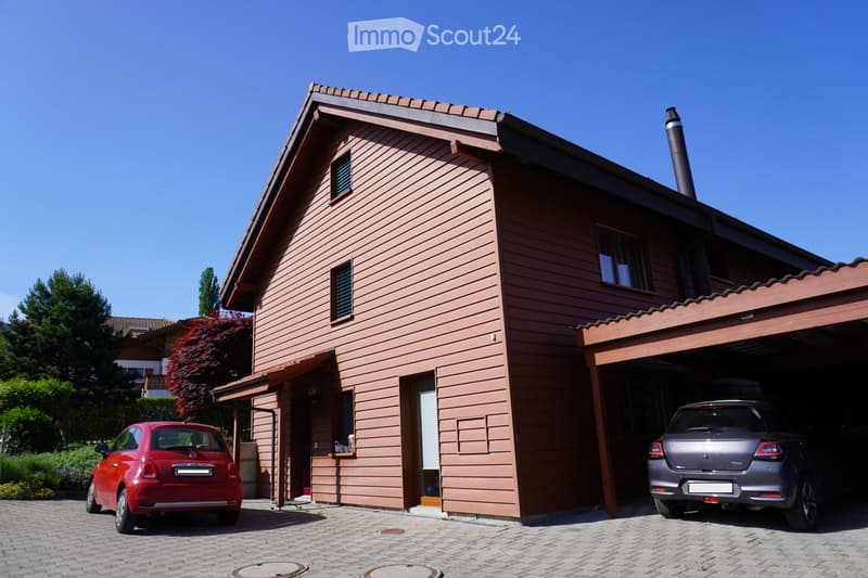 Two-story house with wooden siding, a garage, and a small balcony. Two cars are parked in front.