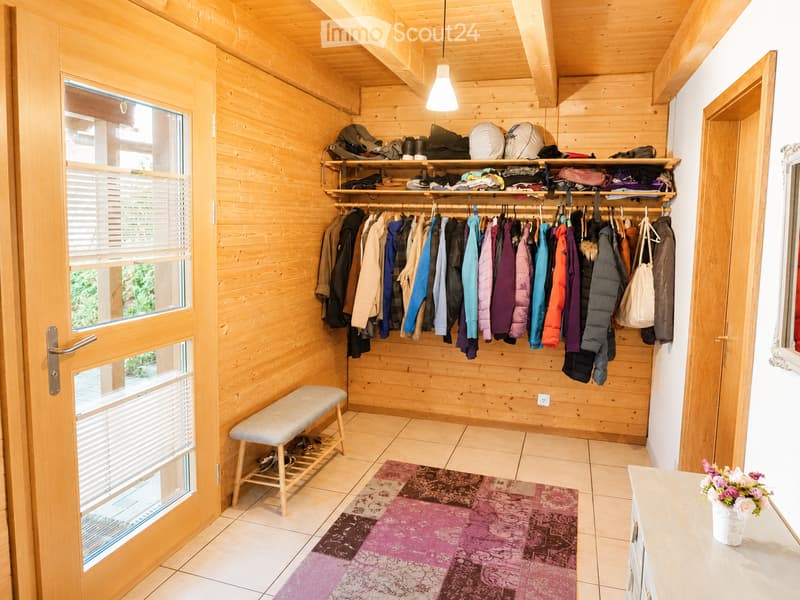 A well-organized hallway with wooden walls, a clothing rack, shelves, a bench, and a colorful rug.