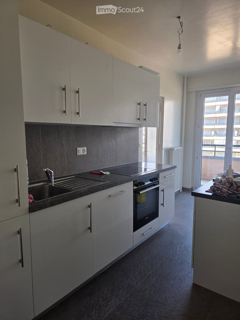 Modern kitchen with white cabinets, dark countertops, stainless steel sink, and built-in oven. Features a window with a view of a balcony.