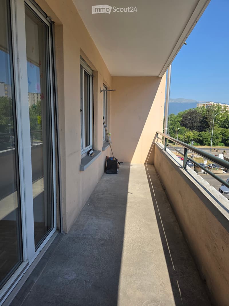 Balcony with concrete floor, metal railing, and windows overlooking a scenic view of the sea and surrounding greenery.