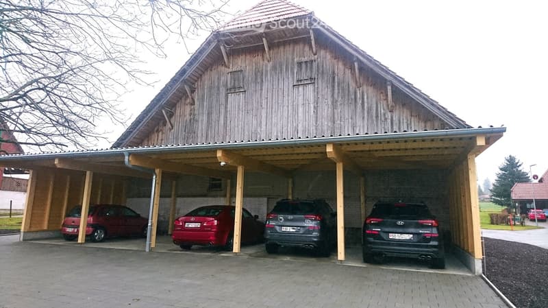 Wooden barn with a carport, 4 cars parked, brick walls, red roof, wooden pillars