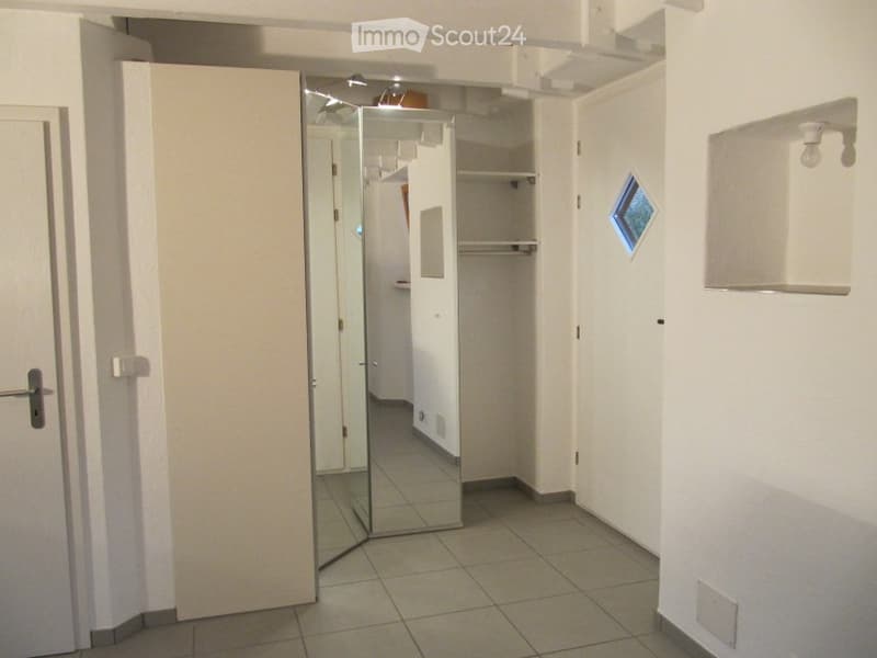 Empty hallway with tiled floor, white walls, a closed door, and a mirrored closet with shelves.