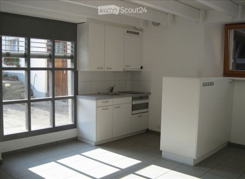 Bright kitchen with white cabinets, a sink, a fridge, and an oven. Large windows allow natural light to fill the space.