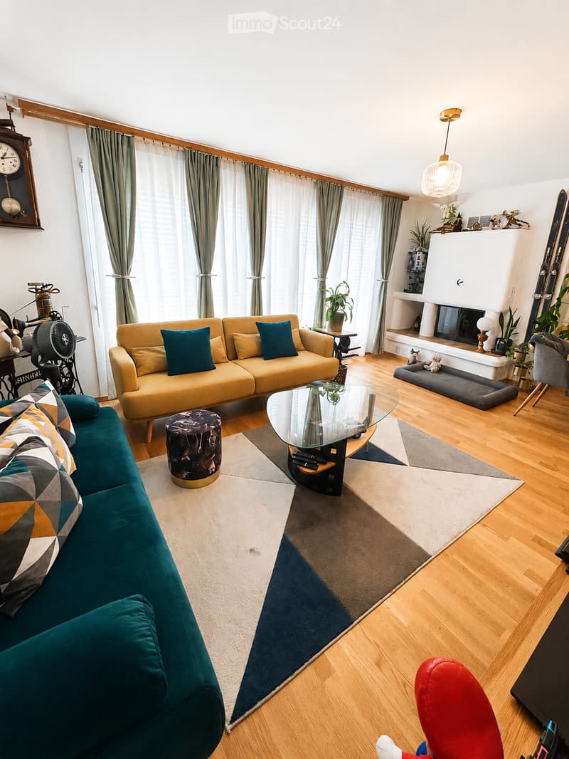 A modern living room with wooden flooring, two sofas, a glass coffee table, a fireplace, and decorative items.