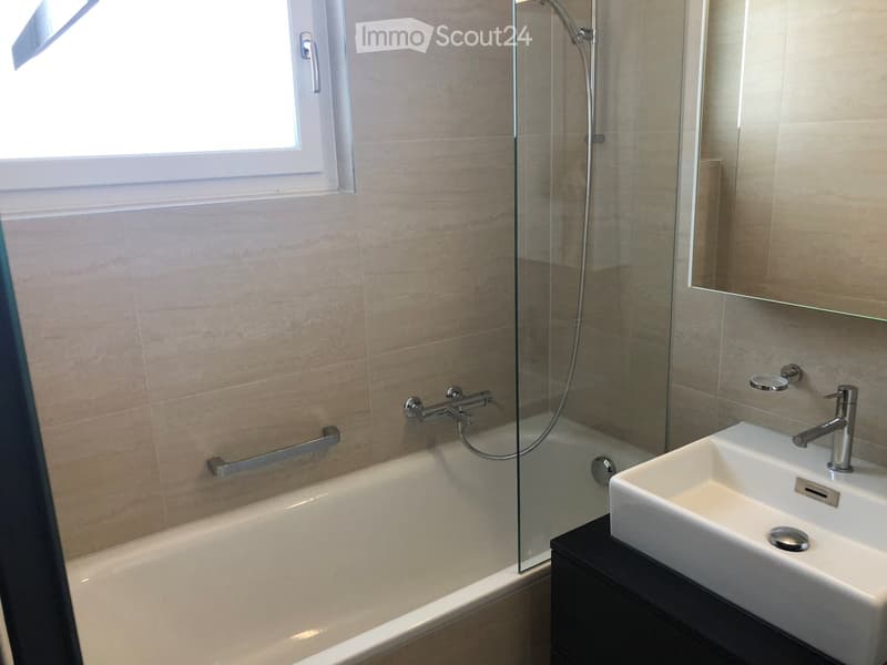 Modern bathroom with a bathtub, glass-enclosed shower, sink, and mirror. Light-colored tiles and chrome fixtures.