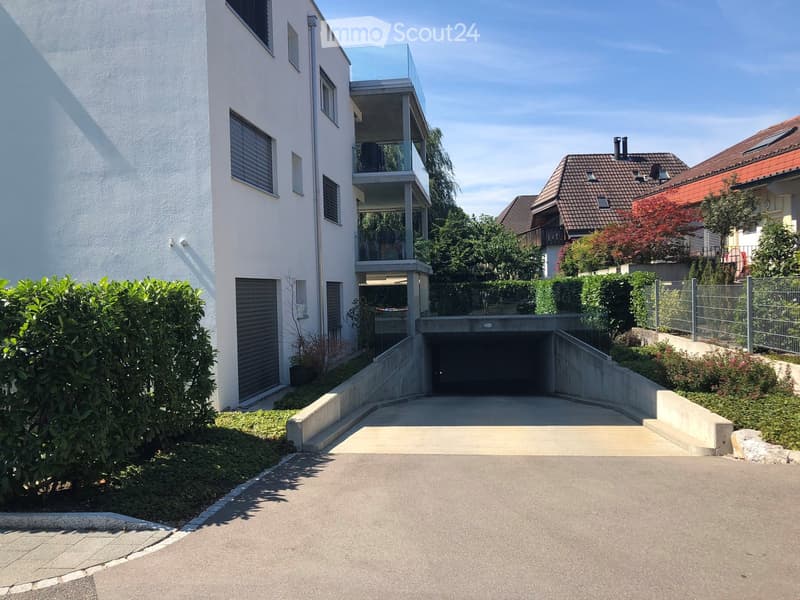 The front exterior of a building with raised ground floor and garage with a concrete ramp.