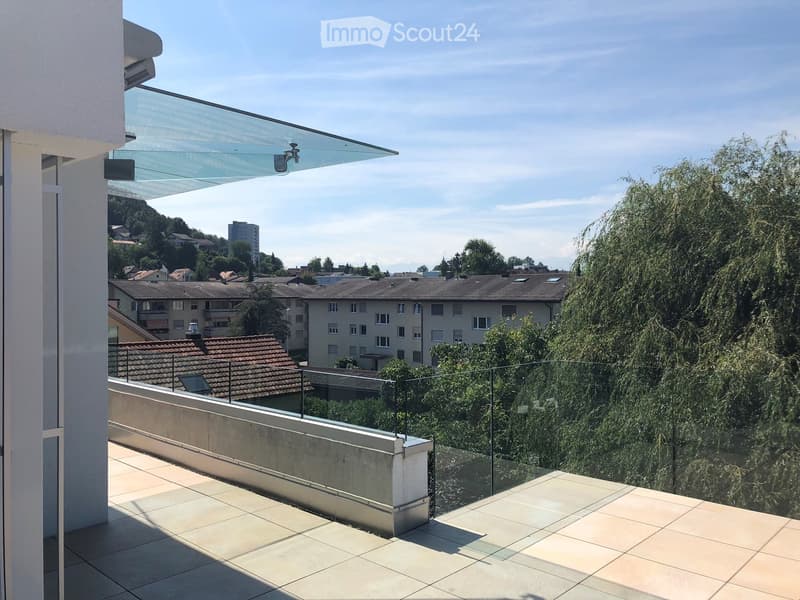 A balcony with tiled floor, glass railings, and a view of the city