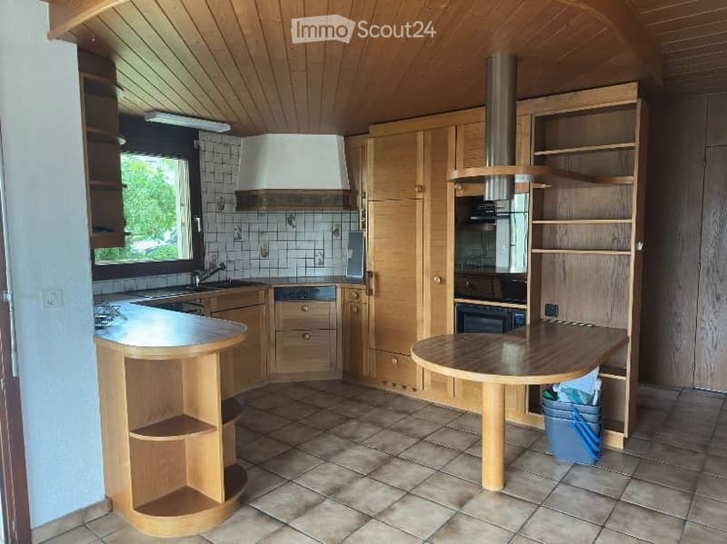Bright kitchen with wooden cabinets, a central island, and a built-in oven. Features include a sink with a faucet, a range hood, and tiled flooring.