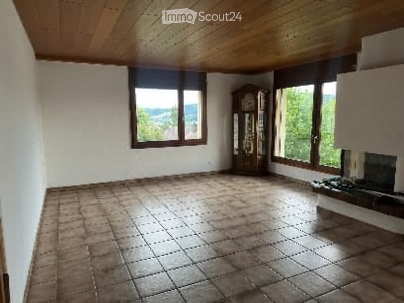 Empty room with wooden ceiling, tiled floor, large windows, and fireplace. No furniture or equipment.