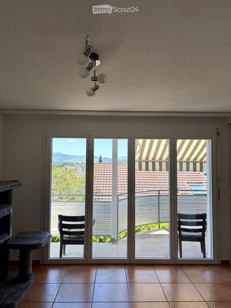 Bright room with large sliding glass doors leading to a balcony, tiled floor, modern chandelier, and a cat tree on the left side.