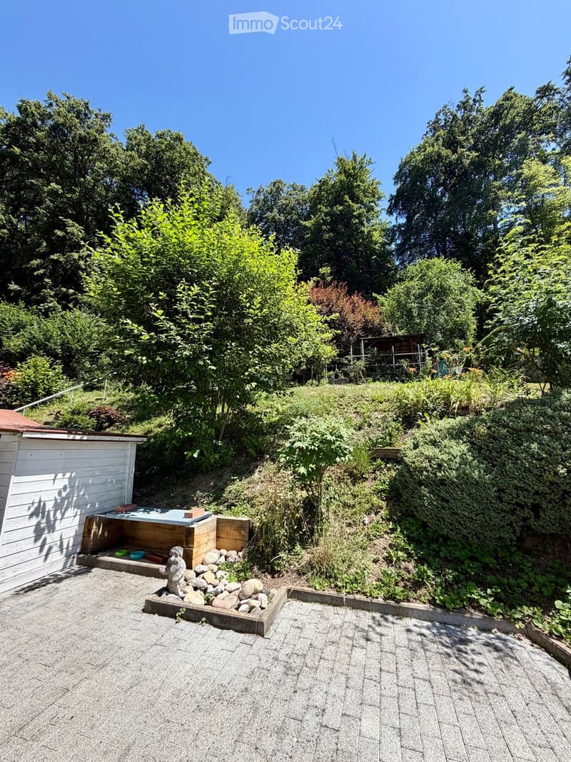 Garden area with gravel pathways, small wooden structure, decorative rocks, and lush greenery.