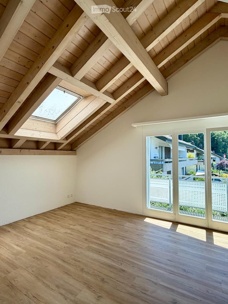 Bright, empty attic room with wooden beams, skylight, and large glass doors leading to a balcony.