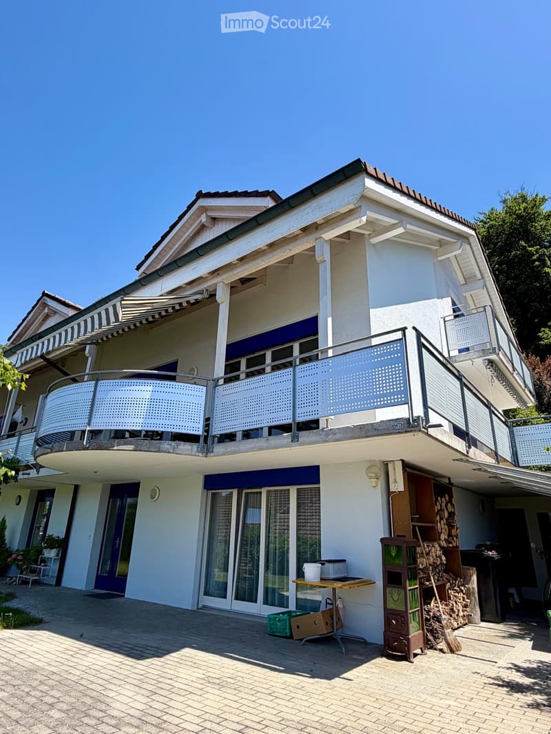 Two-story house with white exterior, blue shutters, balcony with metal railing, and outdoor patio area with a table and chairs.