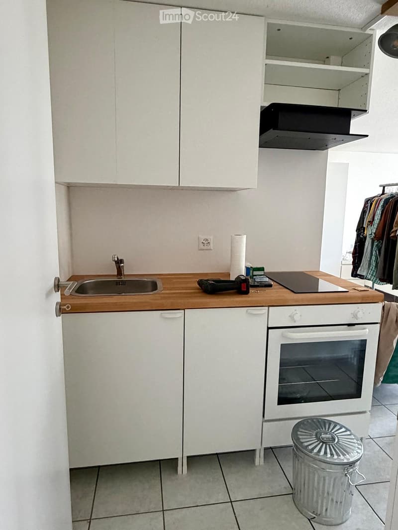 Modern kitchen with white cabinets, wooden countertop, sink, oven, and trash can. Various items are placed on the countertop.