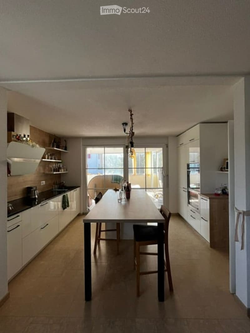 Modern kitchen with white cabinets, a dining table with chairs, and a view through large windows.