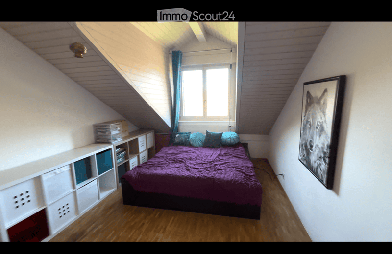Cozy attic bedroom with wooden flooring, slanted ceilings, a bed with purple bedding and multiple pillows, a white storage unit, and a large picture frame on the wall.