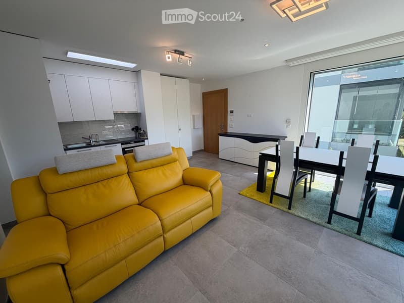 Modern open-plan living and dining area with a yellow leather sofa, dining table with chairs, and a fitted kitchen with cabinets and appliances.