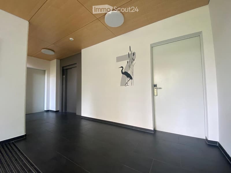 Empty hallway with white walls, black tiled floor, and a wooden ceiling with lights.