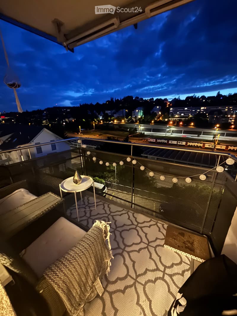 Balcony with a view of the city at dusk, featuring a sofa, small table, and patterned rug.