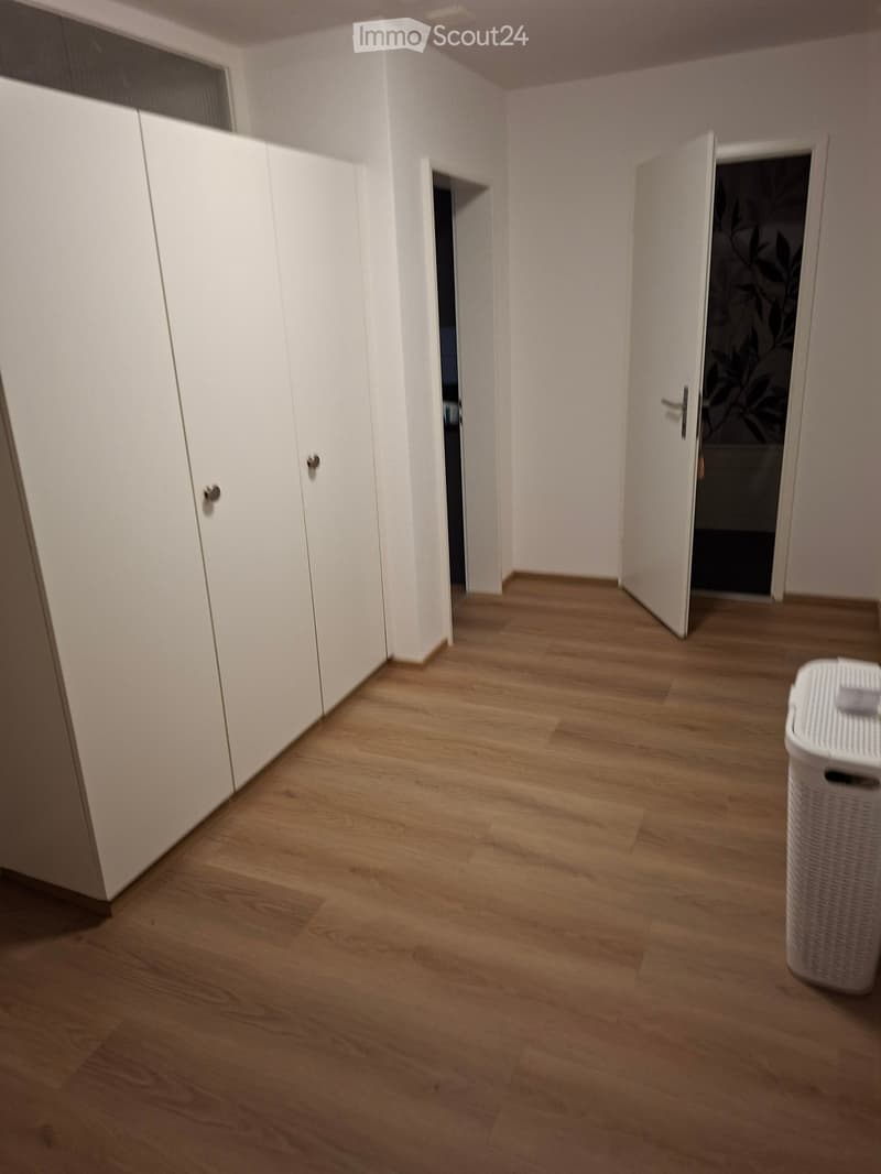 Empty room with wooden flooring, white walls, and white built-in storage units. A laundry basket is visible in the corner.