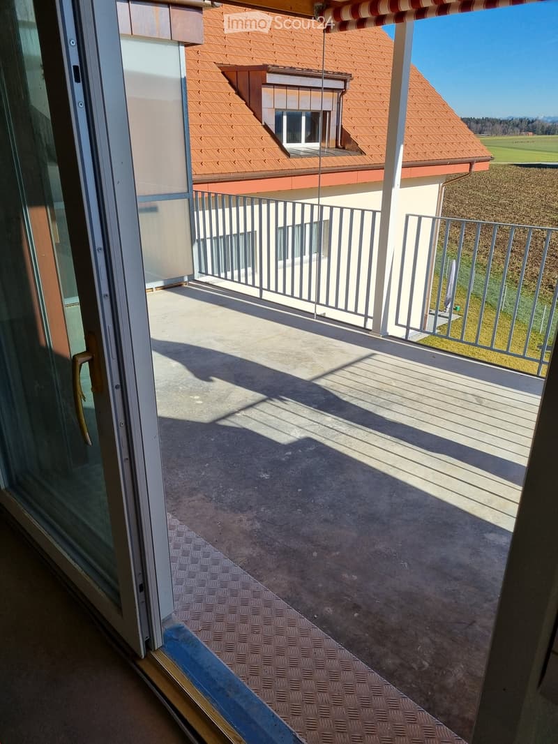Balcony with metal railing, concrete floor, and view of a house with red-tiled roof and surrounding landscape.