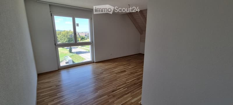 Empty room with wooden flooring and large windows offering a view of the outdoors.