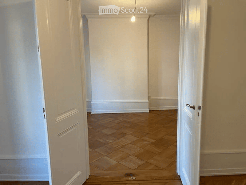 Empty hallway with wooden flooring, white walls, and two open doors leading to adjacent rooms.