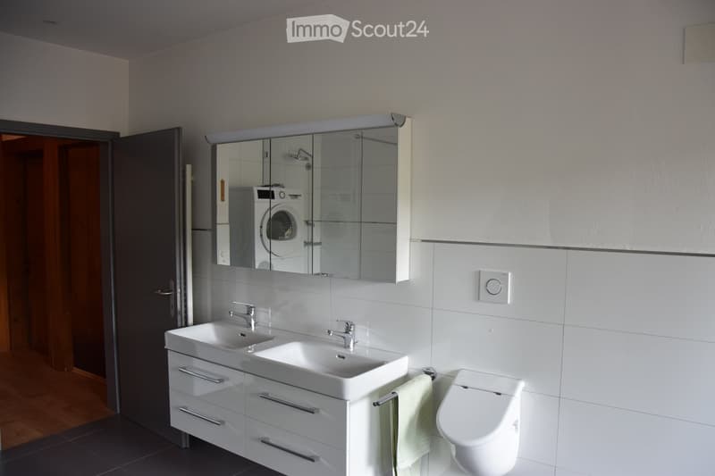 Modern bathroom with a double sink, mirrored cabinet, toilet, and towel hanging on a rack.