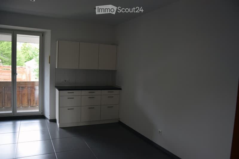 Empty kitchen with white cabinets, black countertops, and tiled flooring. A sliding glass door leads to an outdoor area.