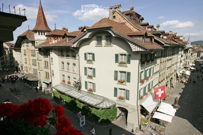 Swiss-style building with brown roof, multiple balconies with flower boxes, multiple levels, street level restaurant entrance.