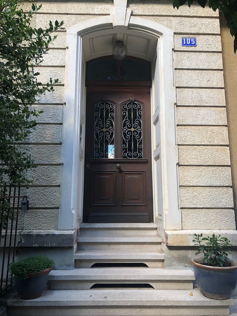 Entrance to a building with a wooden double door, decorative glass panels, steps leading up, and potted plants on either side.