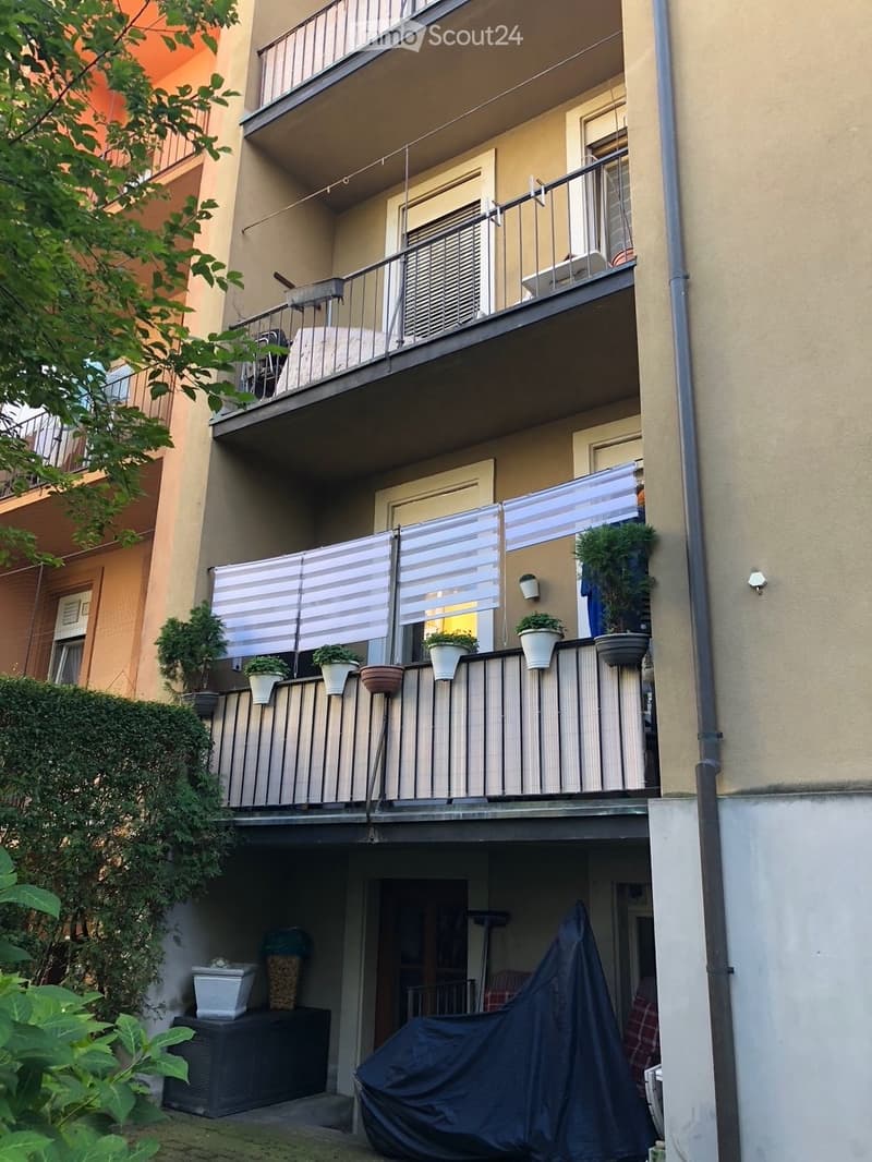 Balcony with white striped blinds, potted plants, and a covered outdoor furniture set.
