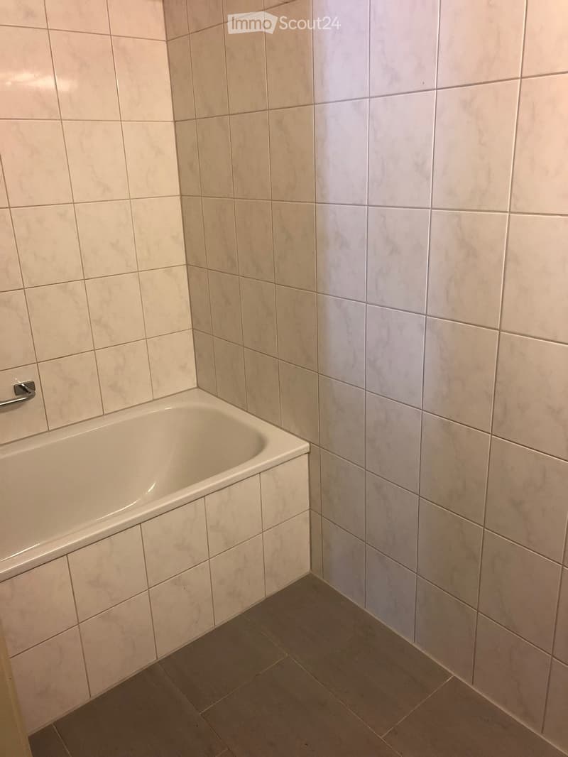 Corner bathtub with tiled walls and floor, featuring a silver grab bar on the left side.