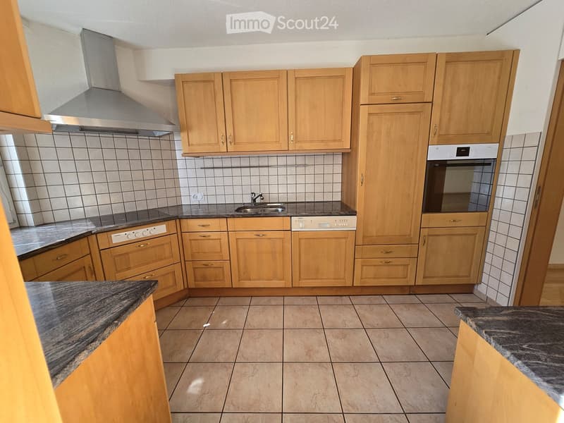 Modern kitchen with light wooden cabinets, granite countertops, tiled backsplash, and stainless steel appliances including a sink, oven, and dishwasher.