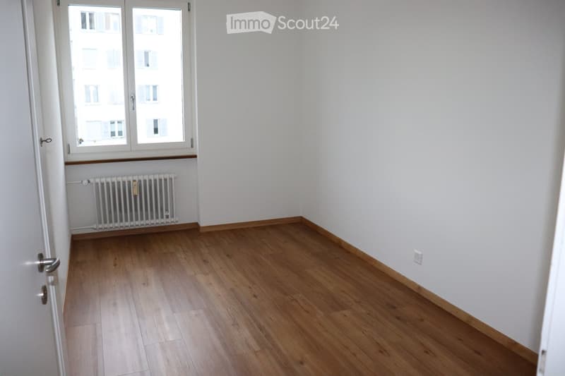 Empty room with light wooden flooring, white walls, a window with white frame, and a radiator below the window.
