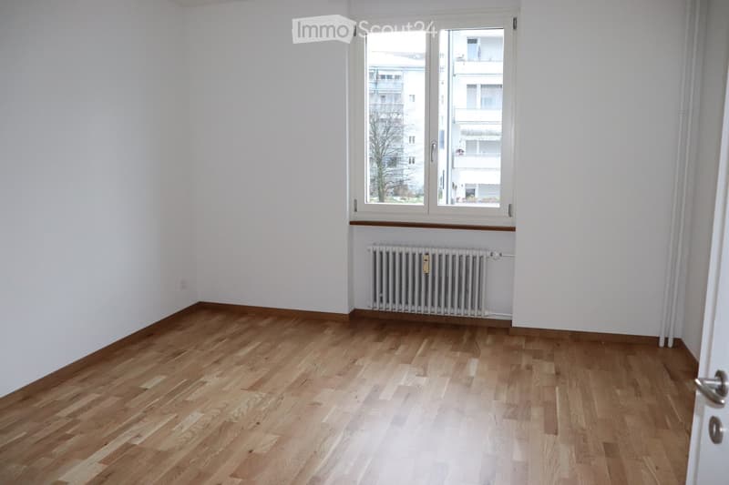 Empty room with light wooden flooring, white walls, and a window with a radiator below it. No furniture or personal items are present.