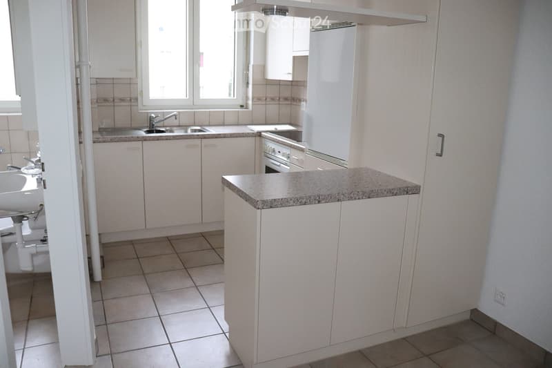 Modern kitchen with white cabinets, granite countertop, stainless steel sink, and built-in appliances including a refrigerator and oven. The space features tiled flooring and ample natural light from large windows.