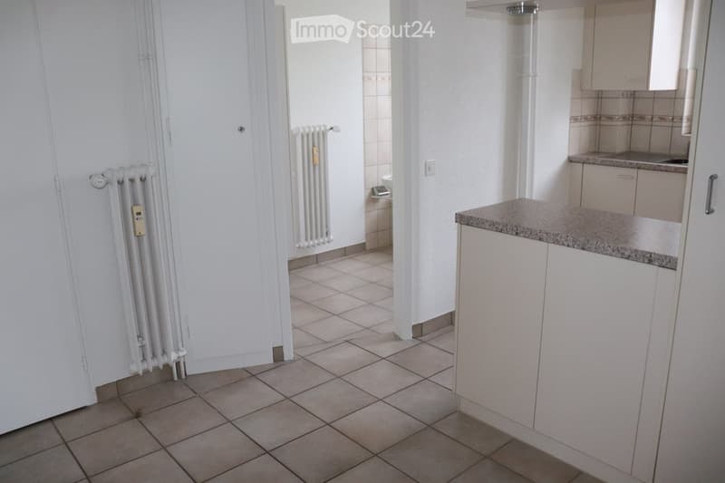 A small, unfurnished kitchen with tiled flooring, white walls, and a countertop with cabinets.