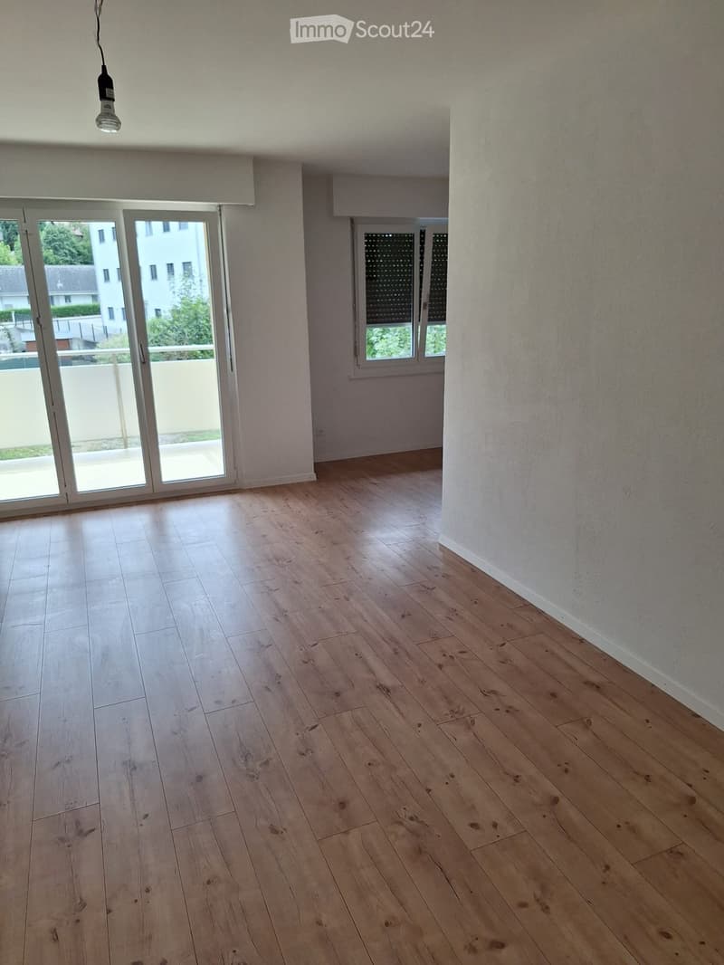 Empty room with light wooden flooring, white walls, large sliding glass door leading to a balcony, and a window with blinds.