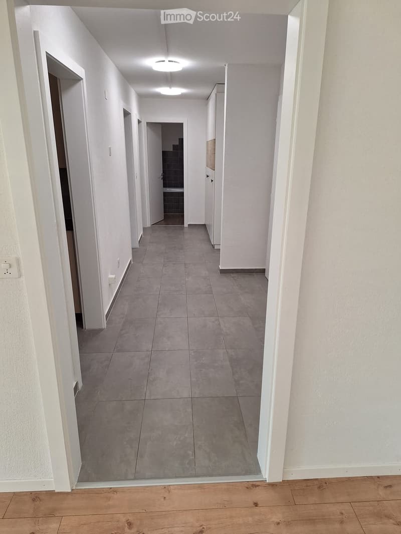 Empty hallway with white walls, grey tiled floor, and several doors leading to other rooms.